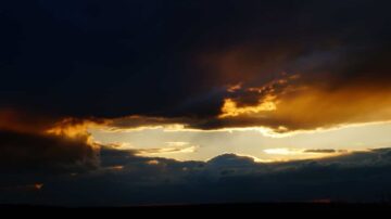 سماء مظلمة مع غيوم داكنة تتخللها أشعة شمس دافئة، تخلق مشهدًا غنائيًا في الأفق. التباين بين الألوان الداكنة والذهبية يضفي جمالًا طبيعيًا على المنظر.