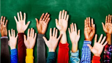 أيدي مرفوعة بألوان مختلفة تتجه نحو الأعلى أمام خلفية خضراء، تمثل التنوع والتفاعل في بيئة تعليمية.