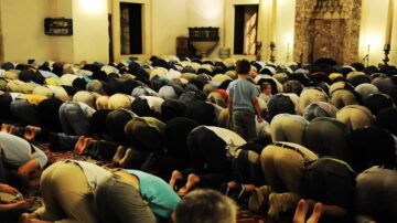 مجموعة كبيرة من الأشخاص يؤدون الصلاة في مسجد، حيث يظهرون في وضع السجود. تركز الصورة على الأعداد الكبيرة من المصلين، مع تفاصيل عن ملابسهم وأرضية المسجد.