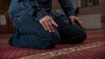 رجل مسلم يؤدي الصلاة على سجادة حمراء، يركع مع يديه على ركبتيه، يظهر التركيز والسكينة في لحظة العبادة.