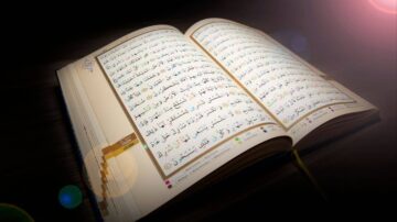 كتاب مفتوح يظهر نص القرآن الكريم مع تفاصيل دقيقة في الخط وتنسيق الألوان، مضاء بإضاءة خافتة تضفي جوًا من الروحانية.