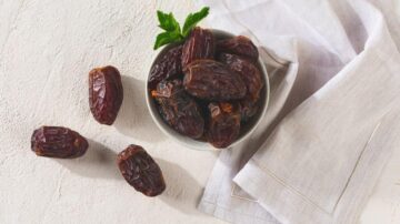 تمر طازج في وعاء صغير مع ورقة نعناع، موضوع على سطح رمادي مع منشفة قطنية بيضاء.