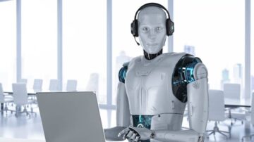 روبوت ذكي يرتدي سماعة رأس ويجلس أمام جهاز كمبيوتر محمول في مكتب حديث، مع نوافذ كبيرة تتيح رؤية المدينة.