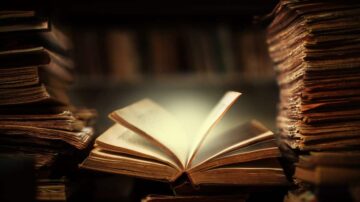 كتاب مفتوح يتوسط مجموعة من الكتب القديمة المكدسة، مع إضاءة خافتة تبرز الصفحات. تعكس الصورة جوًا من الغموض والمعرفة، مما يجذب عشاق القراءة والكتب.