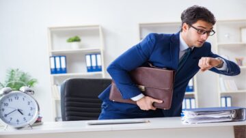 رجل أعمال يرتدي بدلة زرقاء يحمل حقيبة جلدية ويظهر قلقه وهو ينظر إلى ساعته في مكتب عصري. خلفه رفوف تحتوي على ملفات وأدوات مكتبية، وساعة حائط تظهر الوقت.