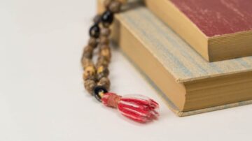 سلسلة من الخرز بجانب كتابين قديمين، أحدهما ذو غلاف أحمر والآخر بألوان زاهية. تبرز السلسلة بتفاصيلها، مما يضيف لمسة جمالية للترتيب.