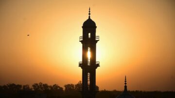 برج مئذنة silhouetted against شمس الغروب في السماء البرتقالية، مع تفاصيل معمارية رائعة.