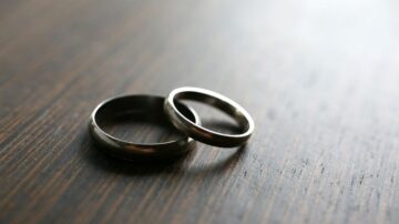 خواتم زفاف معدنية على سطح خشبي داكن، تعكس الضوء بشكل جميل، تمثل الحب والالتزام.