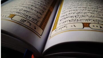 كتاب مفتوح يظهر نصوصًا مكتوبة بخط عربي جميل، مع تفاصيل زخرفية على الحواف. يركز التصوير على الصفحات الداخلية التي تحتوي على آيات من القرآن.