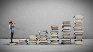 شخص يقف على كومة من الكتب وينظر من خلال منظار، محاط بكومات متزايدة من الكتب تُظهر تقدمًا تدريجيًا. الخلفية جدارية رمادية، مما يبرز الكتب. تُظهر الصورة مفهوم التعلم والنمو الشخصي من خلال القراءة.