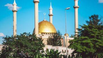 مسجد ذو قبة ذهبية وأبراج طويلة في سماء زرقاء، محاط بأشجار خضراء. يُظهر التصميم المعماري الفريد مزيجًا من العناصر التقليدية والحديثة.