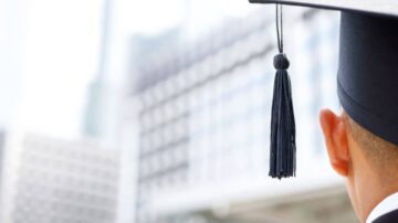 شخص يرتدي قبعة تخرج مع شريطة سوداء، ينظر باتجاه مباني حديثة. توحي الصورة بالاحتفال بالنجاح الأكاديمي والانتقال إلى مرحلة جديدة في الحياة.