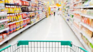 عربة تسوق فارغة في ممر سوبرماركت، مع رفوف مليئة بالمنتجات الغذائية والمشروبات على الجانبين، يظهر الممر بشكل واضح مع إضاءة جيدة.