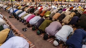 مصلون يؤدون الصلاة في صفوف متراصة داخل مسجد، يظهرون وهم يسجدون مع التركيز على تنوع الملابس وألوانها.