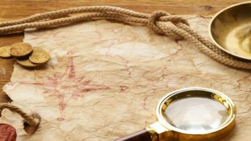 خريطة قديمة مع نجمة حمراء، عدسة مكبرة، وعملات ذهبية، موضوعة على سطح خشبي.