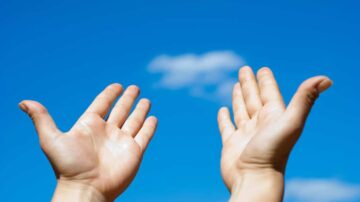 يدين مرفوعتين نحو السماء الزرقاء مع سحابة واحدة في الأفق، تعبر عن الإيجابية والتفاؤل.