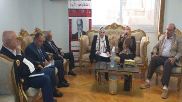 اجتماع لمجموعة من الأشخاص في غرفة مريحة، حيث يجلس ستة أفراد حول طاولة. يتحدث أحدهم بينما يستمع الآخرون بانتباه. تتزين الغرفة بأثاث فاخر، مع وجود لافتة خلفهم تحمل نصًا بالعربية.