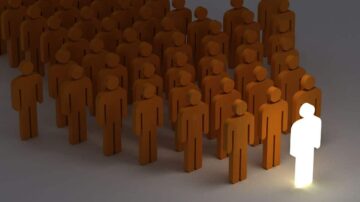 مجموعة من الأشخاص البرتقاليين المصنوعين من شكل رمزي، مع شخص واحد مضئ باللون الأبيض في المقدمة. تعبر الصورة عن التميز والاختلاف بين الأفراد.