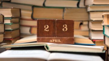 تقويم خشبي يعرض تاريخ 23 أبريل محاط بكتب مرتبة بشكل غير منتظم. تعكس الصورة أجواء القراءة والتعلم.