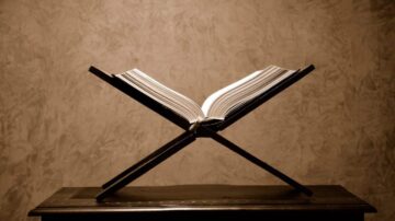 كتاب مفتوح على حامل خشبي مع خلفية ناعمة. يبرز تصميمه الأنيق وتفاصيل الصفحات.