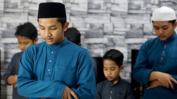 شبان يؤدون الصلاة مع التركيز، يرتدون ملابس تقليدية، خلفية جدارية بألوان محايدة.