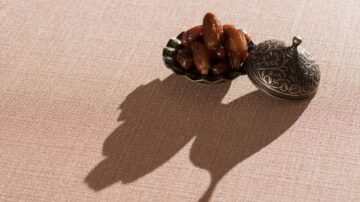 تمر في وعاء معدني مزخرف على قماش بلون وردي، مع ظل مميز يظهر على السطح.