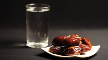 تمر طازج على طبق أبيض بجوار كوب من الماء الشفاف، مع خلفية داكنة. يُظهر المشهد التوازن بين النكهة الطبيعية للتمور والانتعاش الذي يقدمه الماء.