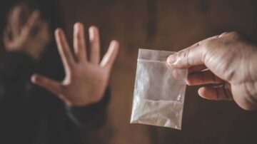 يد تظهر كيسًا شفافًا يحتوي على مادة بيضاء، بينما شخص آخر يمد يده للخلف في حركة رفض. تعبيرات الوجوه تعكس الخوف والقلق في سياق تعاطي المخدرات.