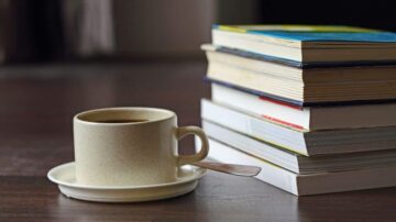 فنجان قهوة بجانب مجموعة من الكتب المكدسة على طاولة خشبية، يبعث على الأجواء الهادئة والمناسبة للقراءة.