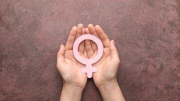 يد تحمل رمز الأنثى الوردي على خلفية رمادية، تعبير عن تمكين المرأة والمساواة بين الجنسين.