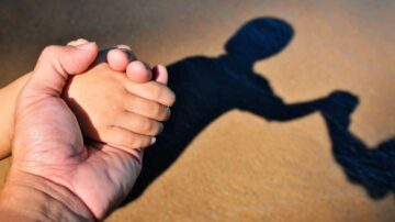 يد كبيرة تمسك بيد صغيرة، بينما يظهر ظل اليدين على الأرض. الصورة تعبر عن الحب والحنان بين الأجيال.