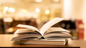 كتاب مفتوح على طاولة خشبية، مع تركيز على الصفحات الداخلية في بيئة مكتبية مضاءة بخفة.