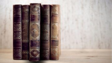 كتب قديمة جلدية ملونة مرتبة على سطح خشبي، مع تفاصيل مزخرفة تبرز جمالها الكلاسيكي.