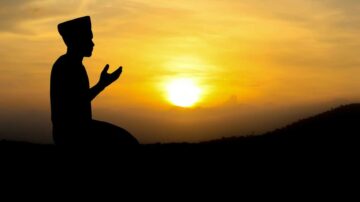 شخص يصلي في الغروب، silhouetted against السماء الذهبية مع أشعة الشمس في الخلفية، يعبر عن التأمل والروحانية في الطبيعة.