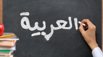 كتابة كلمة "العربية" بخط أبيض على سبورة سوداء، مع وجود تفاح وكتب في الأسفل.