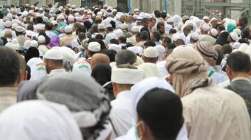 حشد كبير من الحجاج يرتدون قبعات بيضاء خلال أداء مناسك الحج. يظهرون في ساحة مزدحمة بالقرب من الكعبة، مع تنوع في الملابس التقليدية. الأجواء تعكس روح العبادة والتضامن بين المسلمين.