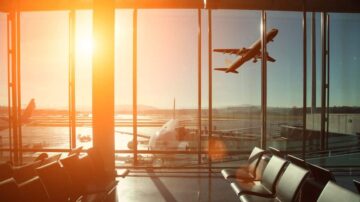 صورة لمطار حديث يظهر فيها طائرات تقلع من مدرج الطائرات خلال غروب الشمس. تمتد المقاعد في المقدمة، بينما تنعكس أشعة الشمس على النوافذ الزجاجية، مما يخلق جوًا مريحًا وهادئًا.
