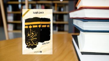 كتاب "رفاء حكاية" لحسن نوريد يظهر على طاولة خشبية مع مجموعة من الكتب. التصميم البسيط للغلاف يتضمن ألوانًا دافئة ونمطًا إبداعيًا، بينما الخلفية تحتوي على رفوف مليئة بالكتب.