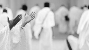 أيدي مرفوعة للدعاء في مكان ديني، مع أشخاص يرتدون ملابس بيضاء في الخلفية. تعكس الصورة روح العبادة والتقرب لله، مما يبرز أهمية الطقوس الدينية في الثقافة الإسلامية.