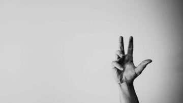 يد مرفوعة تشير بإصبعين في إشارة السلام على خلفية بيضاء. تعبير عن الأمل والتواصل الإيجابي.