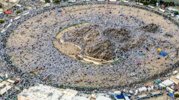 مشهد جوي لآلاف الحجاج في منى خلال مناسك الحج، يظهر الأعداد الكبيرة من الناس يرتدون الملابس البيضاء حول جبل عرفة. يبرز التنظيم الدقيق للحشود والأنشطة الدينية، مما يعكس روح التعاون والعبادة في هذه المناسبة المقدسة.