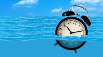 ساعة منبه سوداء تطفو على سطح البحر، مع سماء زرقاء وغيوم بيضاء في الخلفية. تعكس الساعة المياه، مما يخلق تباينًا بصريًا جذابًا.