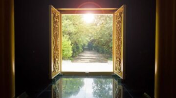 منظر لمدخل مزين بأبواب ذهبية مفتوحة، يكشف عن طريق محاط بالأشجار الخضراء. تسلط أشعة الشمس الضوء على المسار، مما يضفي إحساسًا بالهدوء والجمال. تعكس الأرضية السوداء لمسة من الأناقة.