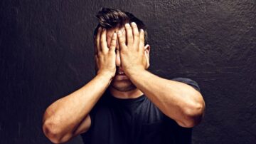 رجل يغطي وجهه بيديه، يعبر عن الإحباط أو القلق، خلفية داكنة تضيف شعورًا بالتوتر.
