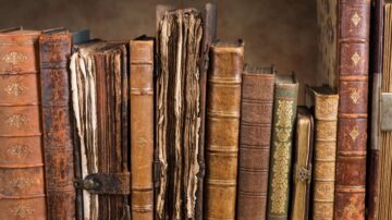 كتب قديمة مصفوفة على رف، تظهر تفاصيل غلافها الجلدي وتجاعيد الصفحات، تعكس تاريخاً غنياً وثقافة أدبية.