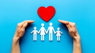 يد تحتوي على عائلة مكونة من أربعة أشخاص ورمز قلب أحمر، خلفية زرقاء. تعبير عن الحب والاهتمام بالعائلة.