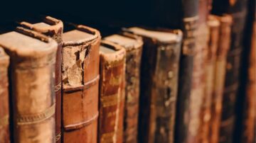 كتب قديمة مرتبة على رف، تظهر تفاصيل الغلاف والتآكل، تعكس تاريخها الغني.