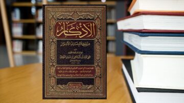 كتاب "الأذكار" للنووي مع تغليف مزخرف، موضوع على طاولة خشبية، خلفية من مكتبة تضم مجموعة من الكتب.