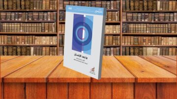 كتاب "ماجد الإنسان" يظهر في المقدمة على طاولة خشبية، مع خلفية تحتوي على رفوف مكتبية مليئة بالكتب القديمة. الكتاب يحمل غلافًا ملونًا بتصميم هندسي بسيط ورقم 488 في الزاوية العلوية.