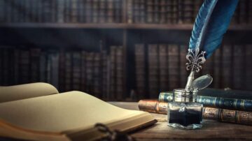 حبر وزجاجة حبر بجانب كتاب مفتوح وكتب قديمة في خلفية مكتبة. الريشة الزرقاء تبرز بجانب زجاجة الحبر، مما يضفي طابعاً أدبياً على المشهد.